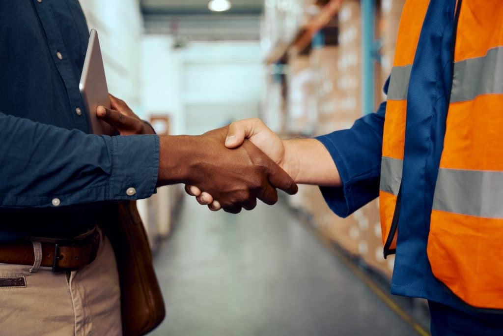 Midsection view of two male workers shaking hands at factory