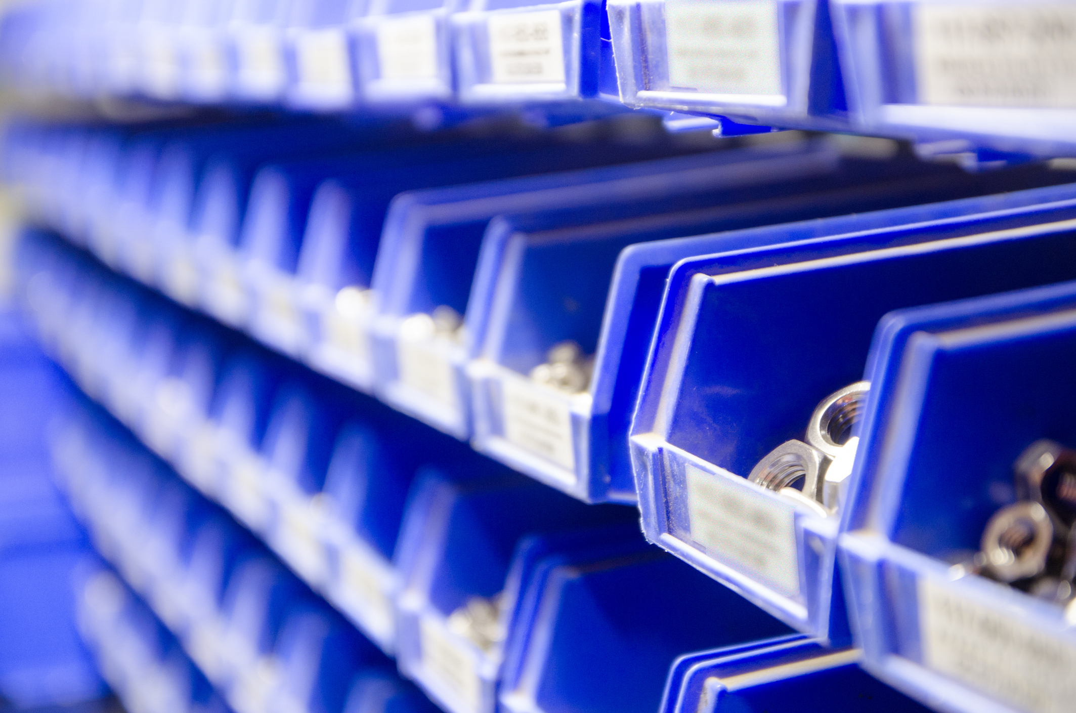 Rows blue plastic storage bins containing screws, bolts and nuts.