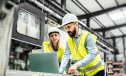 A portrait of a mature industrial man and woman engineer with laptop in a factory, working.